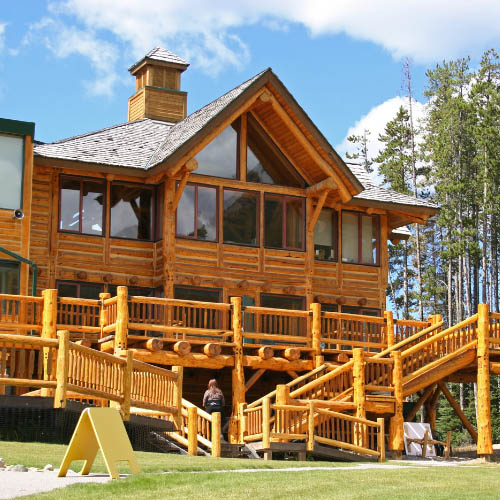 A large wooden house with a sloped roof, surrounded by trees and a clear blue sky